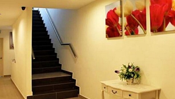 A staircase leading to a landing with a wall-mounted light fixture and a small table with a vase of flowers. - One Hotel Lintas Jaya (Kota Kinabalu)