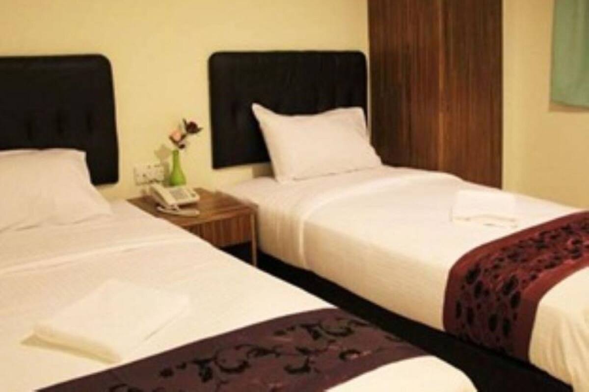 A hotel room with two single beds, a nightstand with a phone and a vase of flowers, and a wooden headboard.