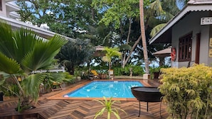 Un espace piscine doté d’une terrasse en bois, entouré de plantes tropicales et d’un palmier.