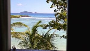 Une vue d’une plage tropicale avec une eau d’un bleu limpide, des palmiers et une île lointaine.