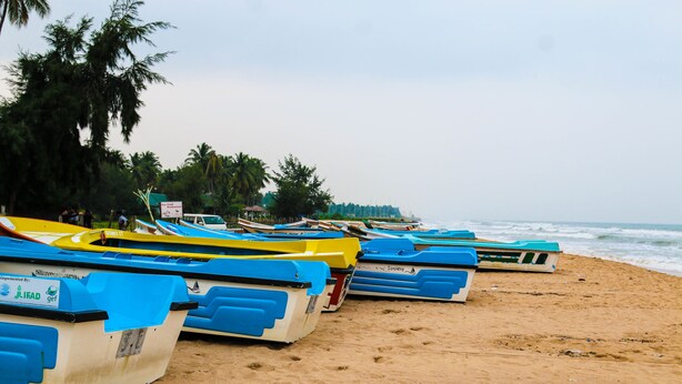 Une rangée de bateaux aux couleurs vives sur une plage de sable, avec une enseigne d’hôtel au premier plan.