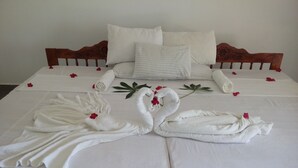 Un lit parfaitement fait, avec des draps blancs, deux serviettes en forme de cygne et des pétales de rose éparpillés.
