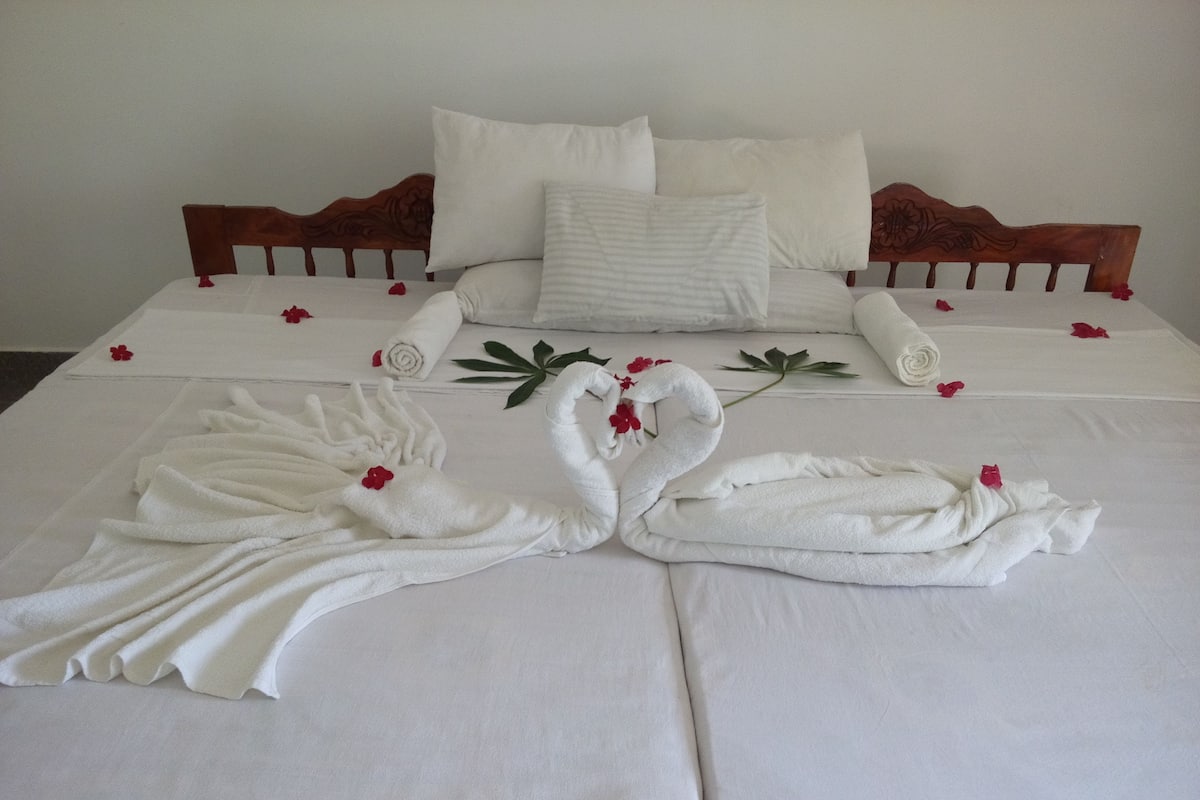 Een net opgemaakt bed met witte lakens, twee handdoeken in de vorm van zwanen en losse rozenblaadjes.
