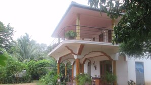 Une maison à deux étages avec un balcon, entourée de verdure.