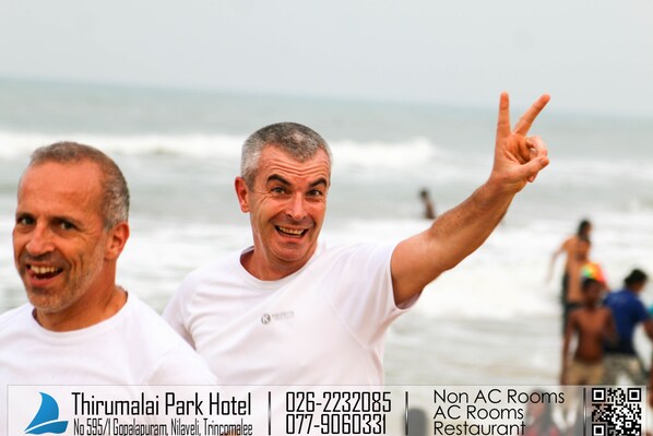 Two men at a beach with a hotel sign in the background.