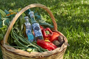 A wicker basket filled with vegetables and two bottles of olive oil on a grassy surface.
