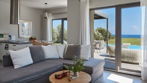 A modern living room with a gray sectional sofa, a round coffee table with a violin and flowers, and a large sliding glass door leading to a pool area with outdoor furniture.
