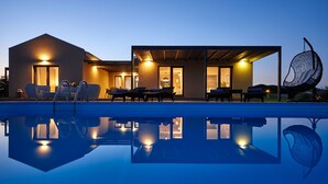 A modern house with a swimming pool, outdoor seating, and a hanging chair.