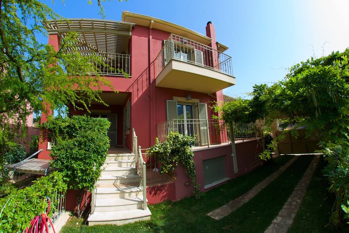 Une maison à deux étages dotée d’un balcon, d’un escalier et d’un jardin bien entretenu.