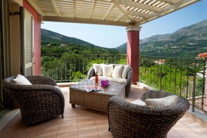 Un balcon agrémenté de meubles en osier, d’une table basse en verre et d’un magazine. Le balcon offre une vue sur un paysage montagneux.