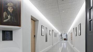 A long, well-lit hallway with framed artwork on the walls, leading to a door at the end.