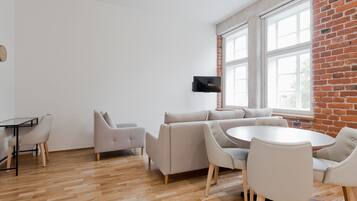A modern living room with a brick wall, a flat-screen TV mounted on the wall, a round dining table with chairs, and a sofa.