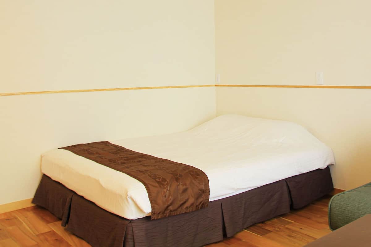 A single bed with a brown bedspread and white sheets, a green sofa, and a wooden floor.