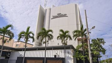 A hotel named Sunset Terrace with a modern design, featuring a prominent sign and a series of palm trees in front.