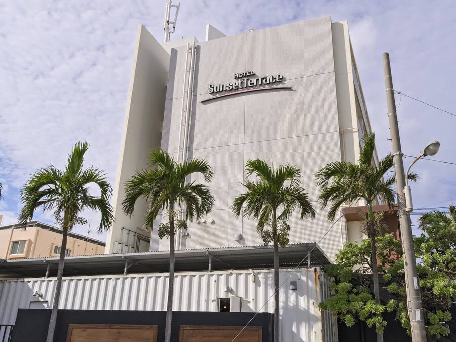 A hotel named Sunset Terrace with a modern design, featuring a prominent sign and a series of palm trees in front.