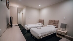 A hotel room with two beds, a desk, a chair, a nightstand with a lamp, and a television. - CityLights Hotel (Perth)