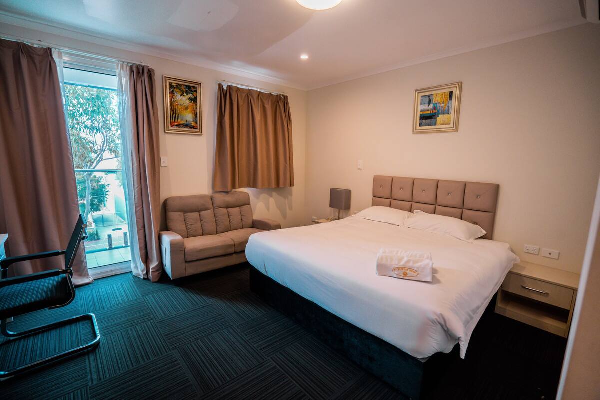 A hotel room with a bed, a chair, a desk, and a window with curtains.