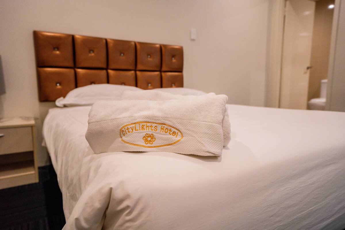 A hotel room with a neatly made bed, a headboard with a tufted design, and a towel with the hotel name on it.