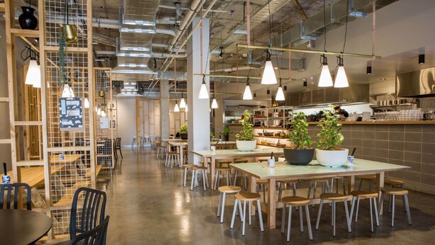 A modern restaurant with high ceilings, exposed ductwork, and pendant lighting. Tables are arranged with stools, and there are potted plants on the tables. - CityLights Hotel (Perth)