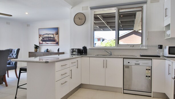 A modern kitchen with white cabinetry, a built-in dishwasher, a microwave, and a large window providing natural light. - Ivy Units Glen Waverley (Glen Waverley)