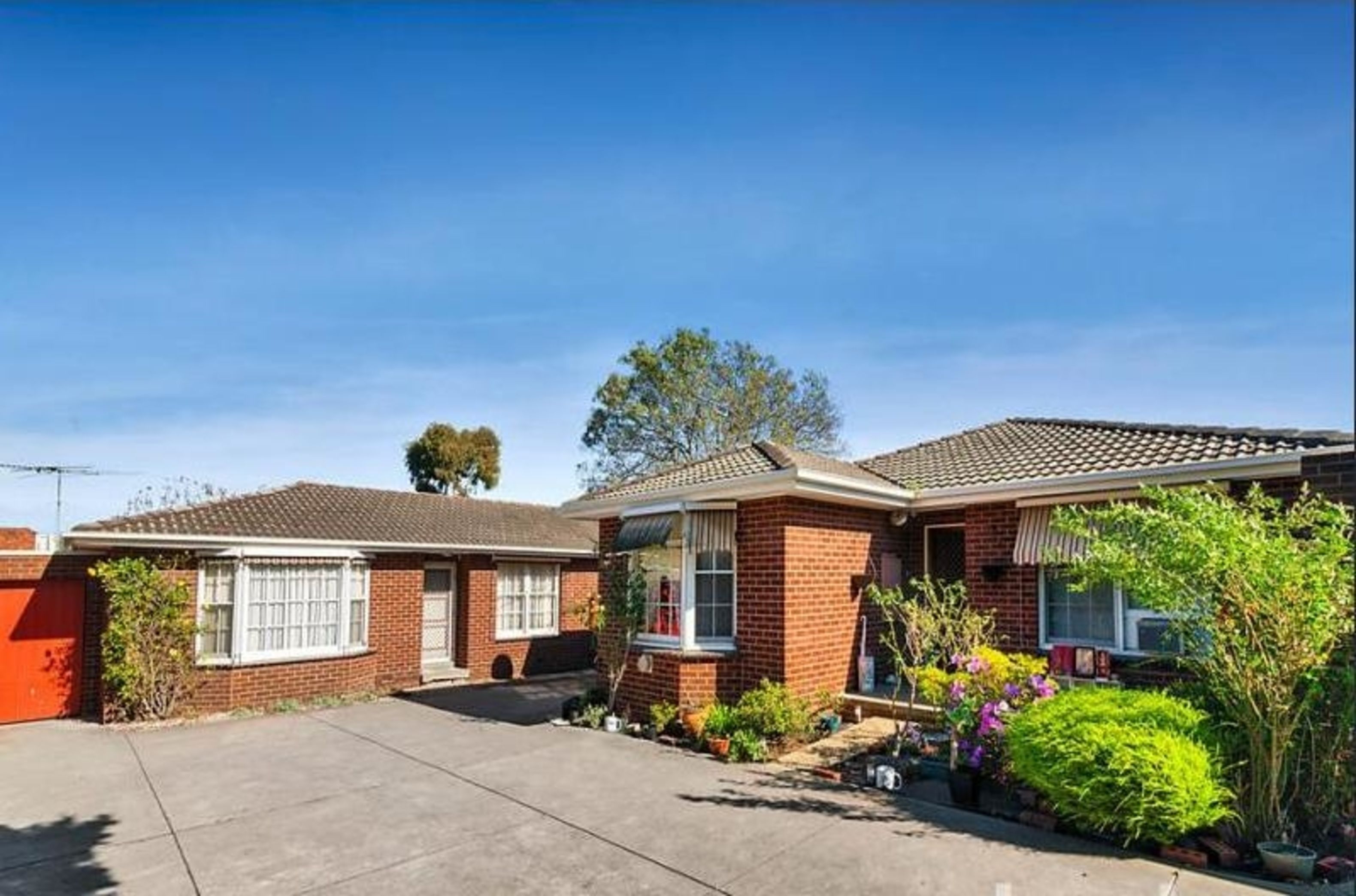 A two-story brick house with a front driveway, a garage, and a well-maintained garden with various plants and flowers.
