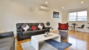 A modern living room with a black leather sofa, white coffee table, and a large window providing natural light. - Ivy Units Glen Waverley (Glen Waverley)