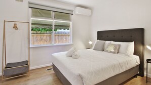 A bedroom with a large bed, a window with a view of greenery, a hanging rack, and a bedside lamp. - Ivy Units Glen Waverley (Glen Waverley)