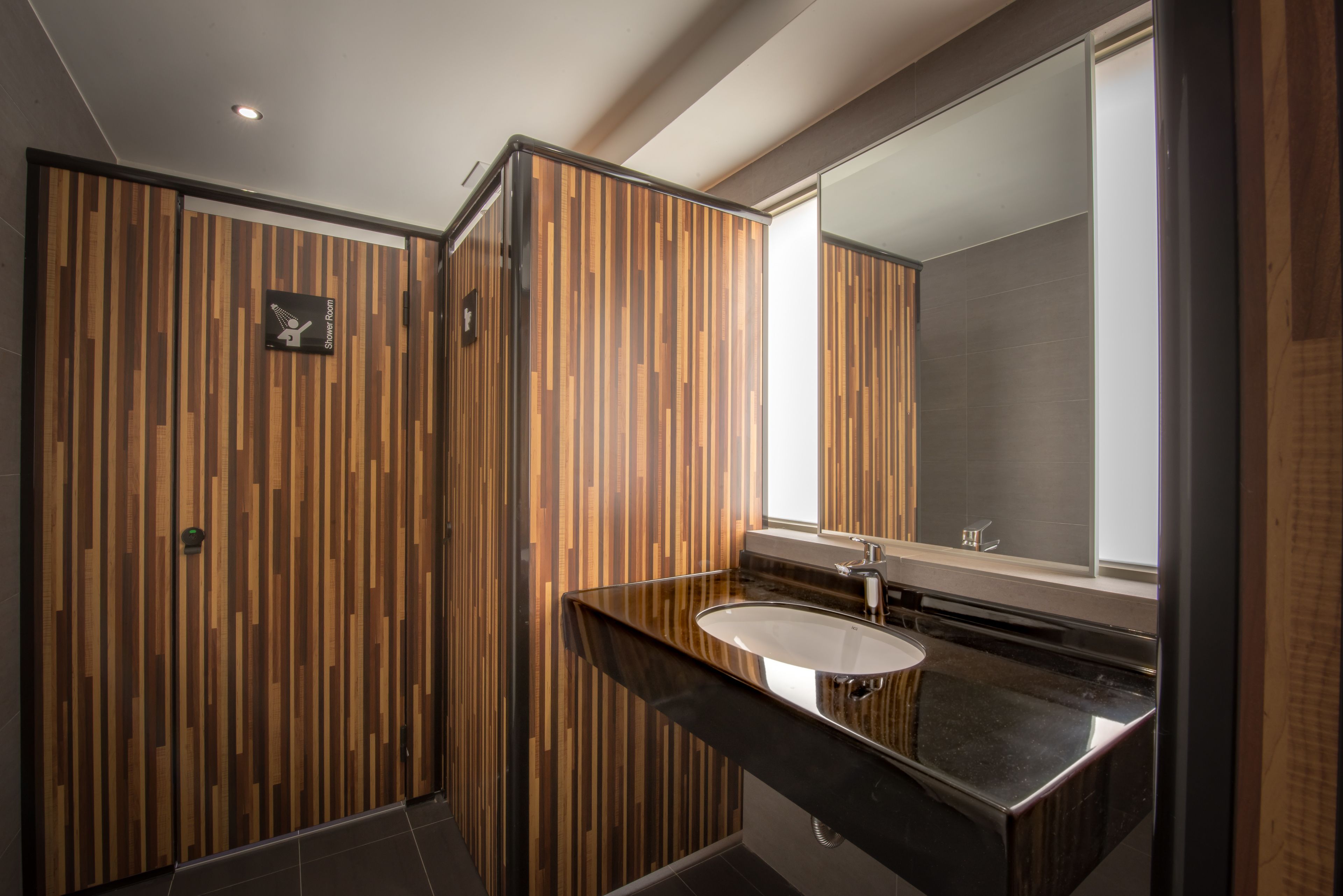 Un baño moderno con pared de paneles de madera, encimera negra y un espejo grande.