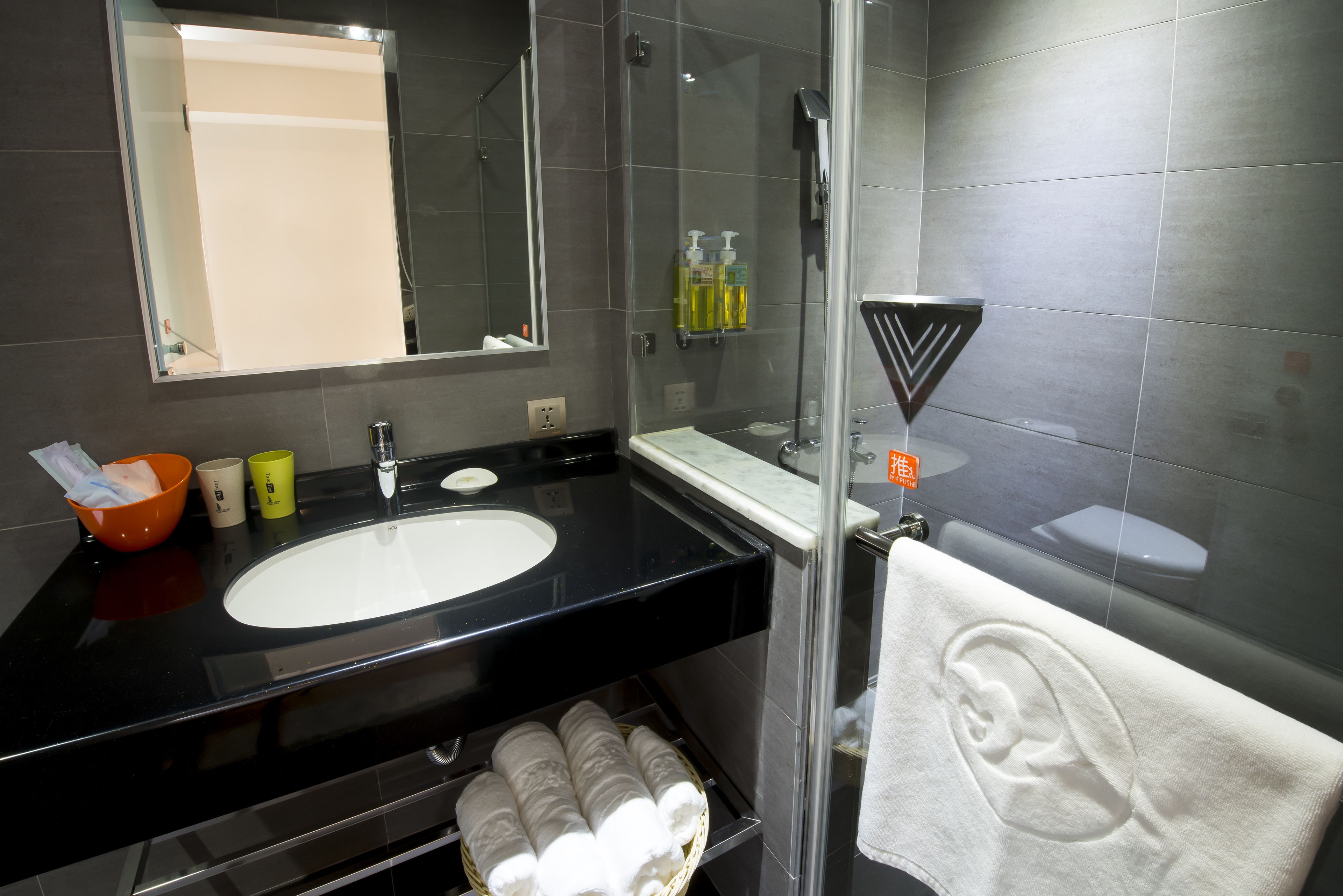A modern bathroom with a black sink, a mirror, a glass shower enclosure, and a towel with an ear design.