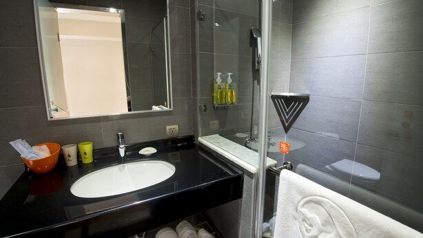 A modern bathroom with a black sink, a mirror, a glass shower enclosure, and a towel with an ear design. - Legend Hotel Pier 2 (Kaohsiung)