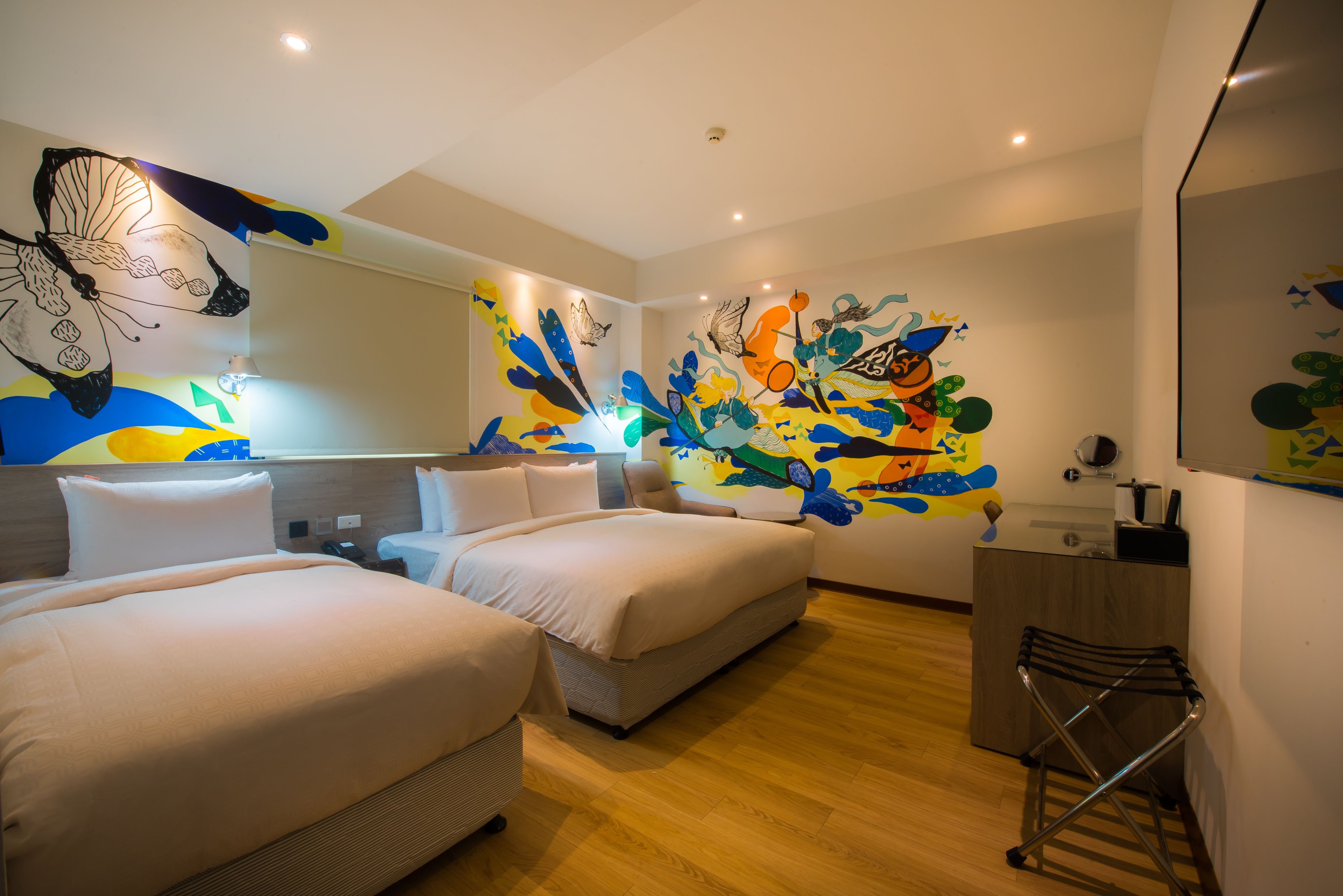 A hotel room with two beds, a desk, and a mirror.
