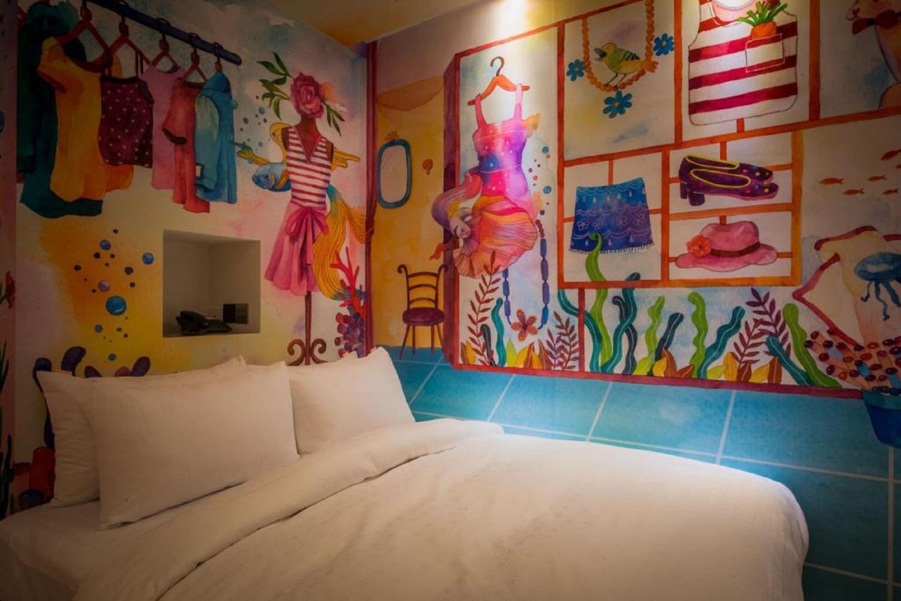 A bedroom with a bed, colorful wall art, and a blue-tiled shower area.
