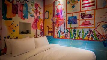 A bedroom with a bed, colorful wall art, and a blue-tiled shower area.