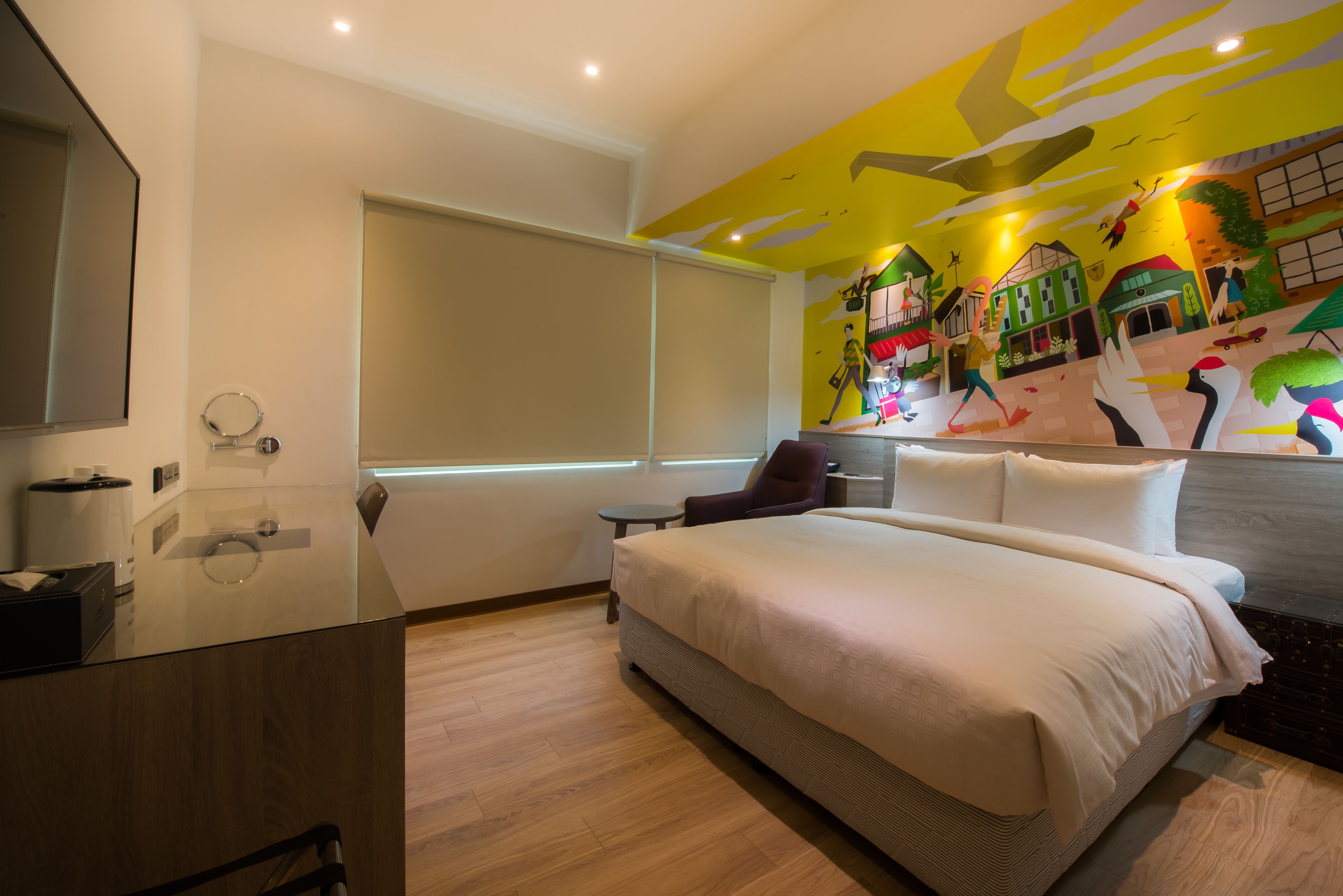 A modern hotel room with a large bed, a small desk, a chair, and a window.