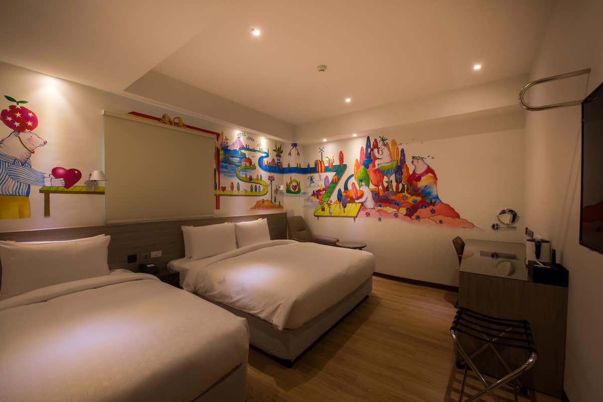 A hotel room with two beds, a desk, a chair, and a colorful abstract mural on the wall.