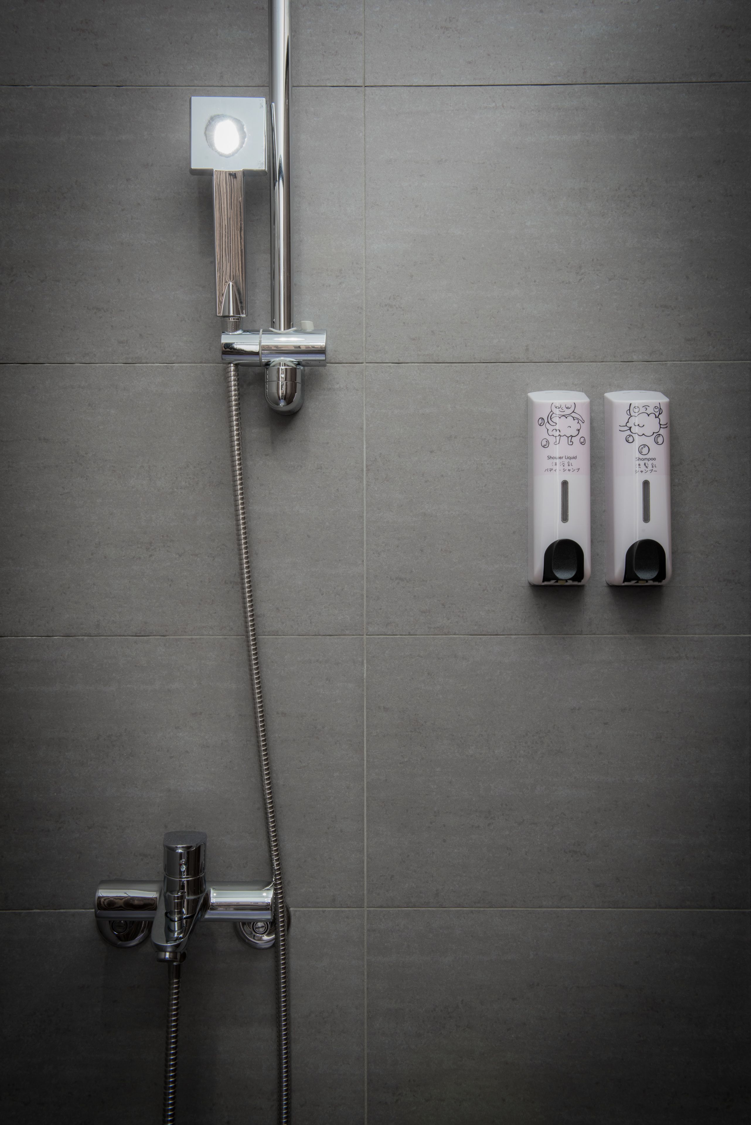 Un baño moderno con ducha de cromo, cabezal de ducha de mano y dos dispensadores de jabón fijos en la pared.