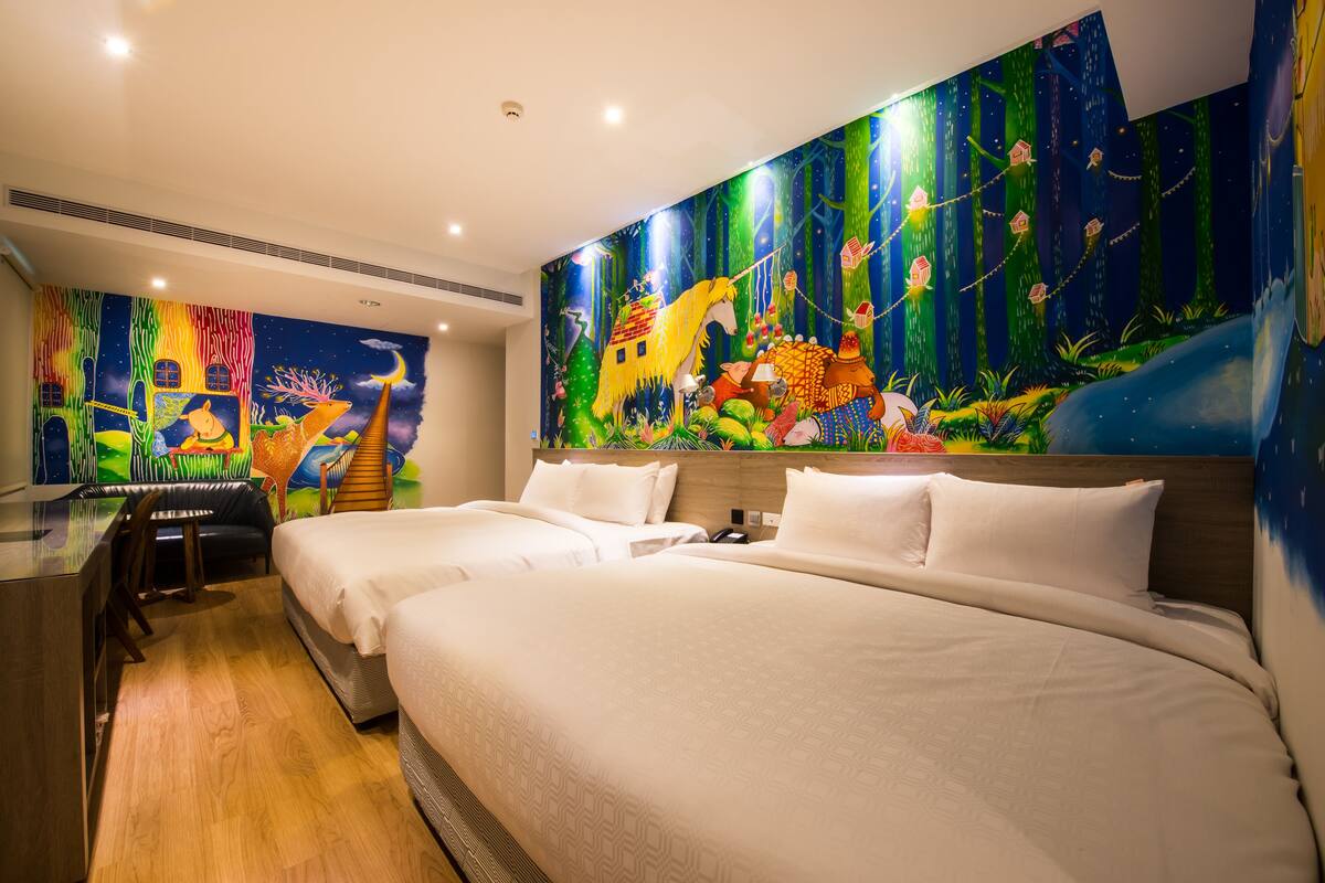 A hotel room with two beds, a desk, and a large mural on the wall.