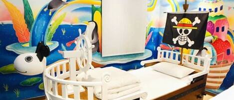 A child's room with a bed shaped like a pirate ship, a mural with sea creatures, and a skull and crossbones flag.