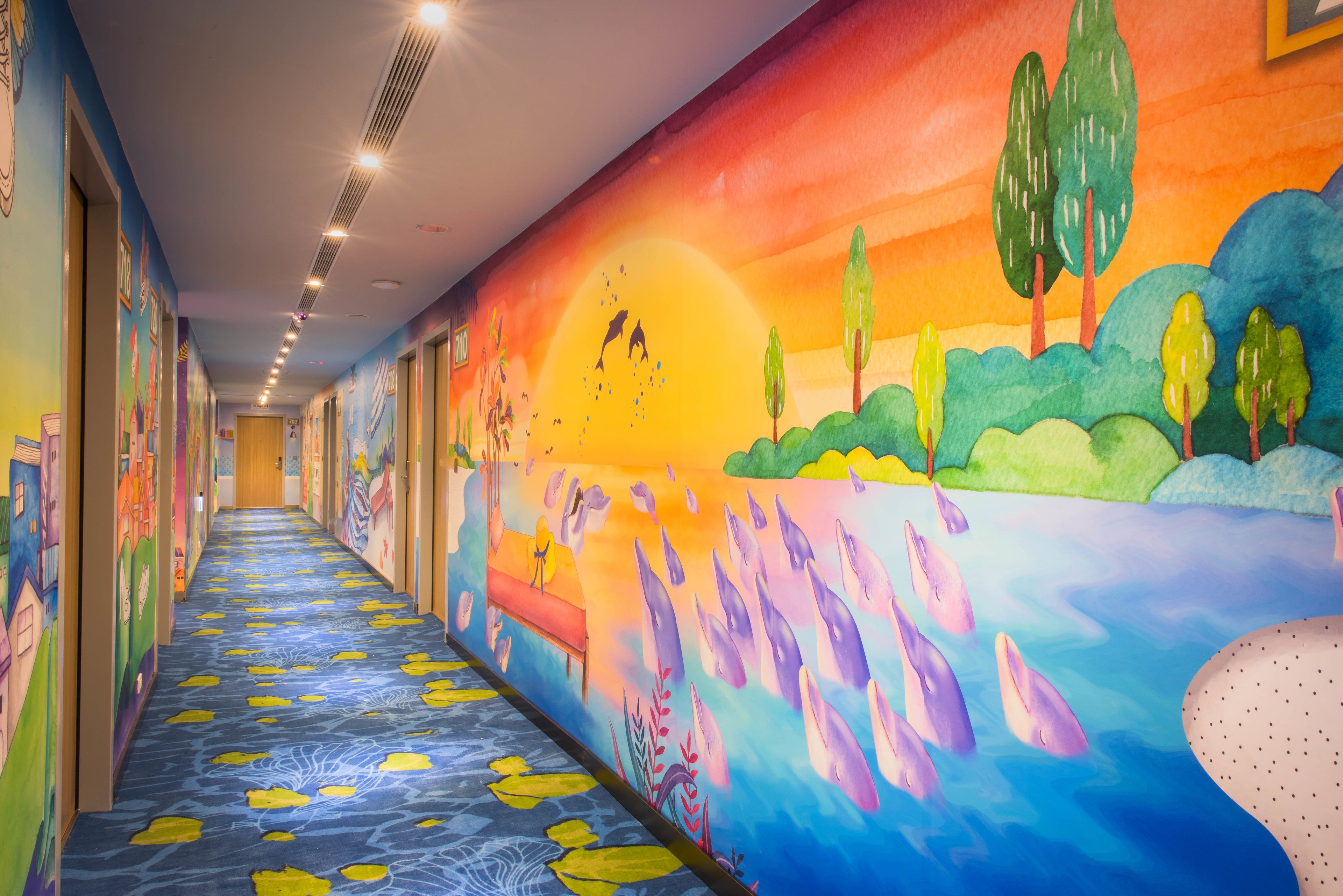 Un pasillo de colores brillantes con un mural que representa un atardecer sobre un cuerpo de agua, con delfines, árboles y un banco.