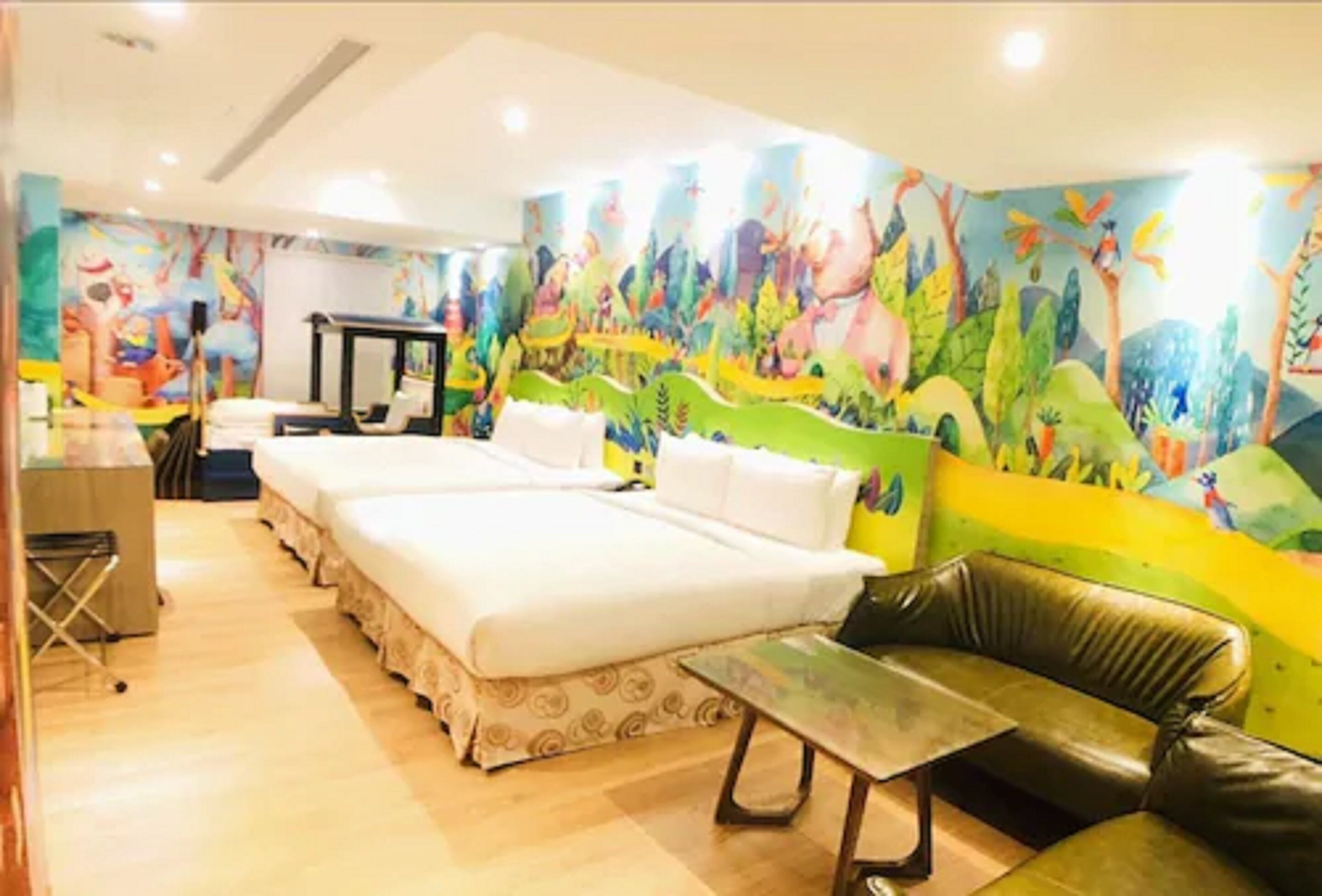 A hotel room with a large bed, a sofa, a small table, and a mural on the wall.