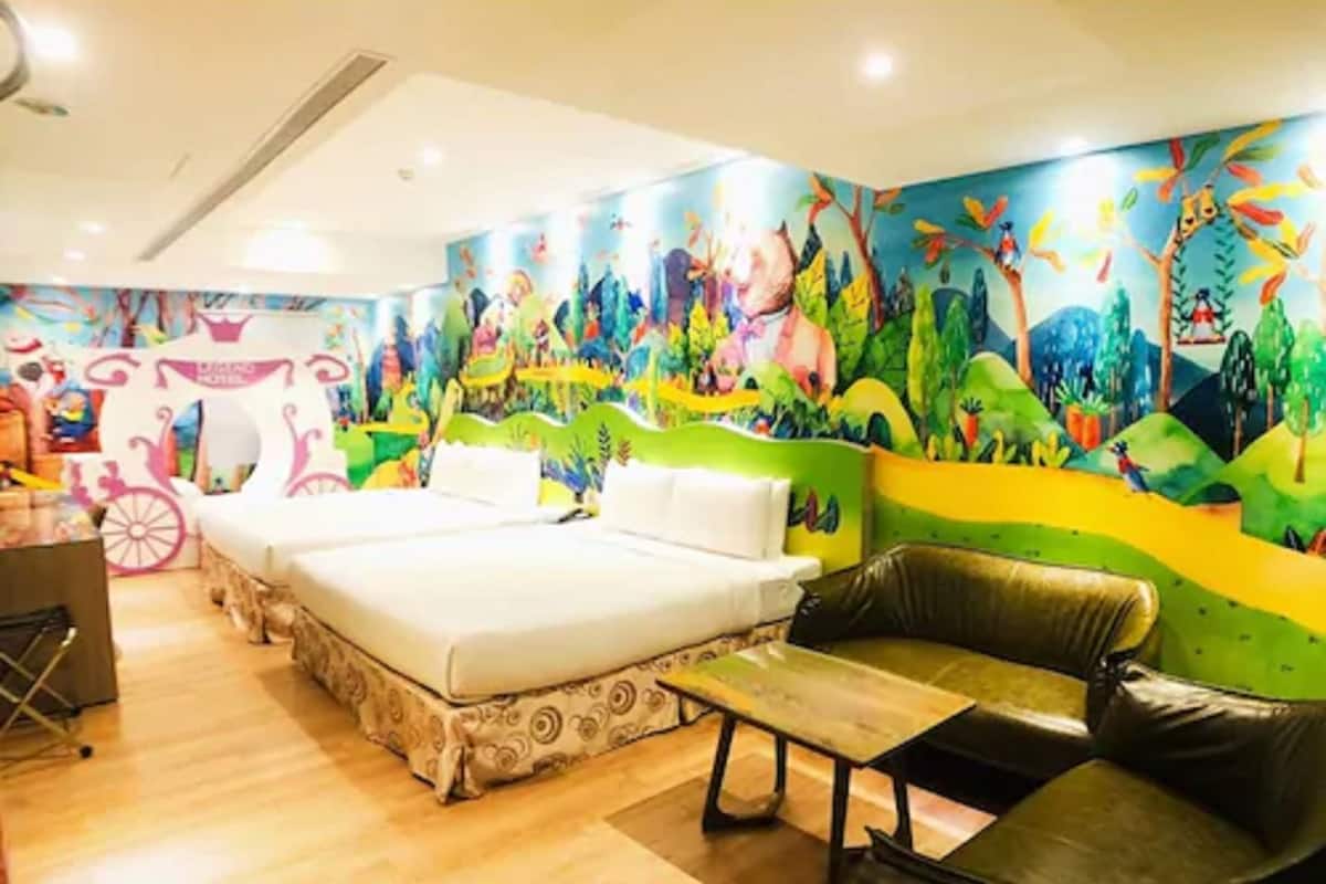 A hotel room with a bed, a green sofa, a small table, and a colorful mural on the wall.