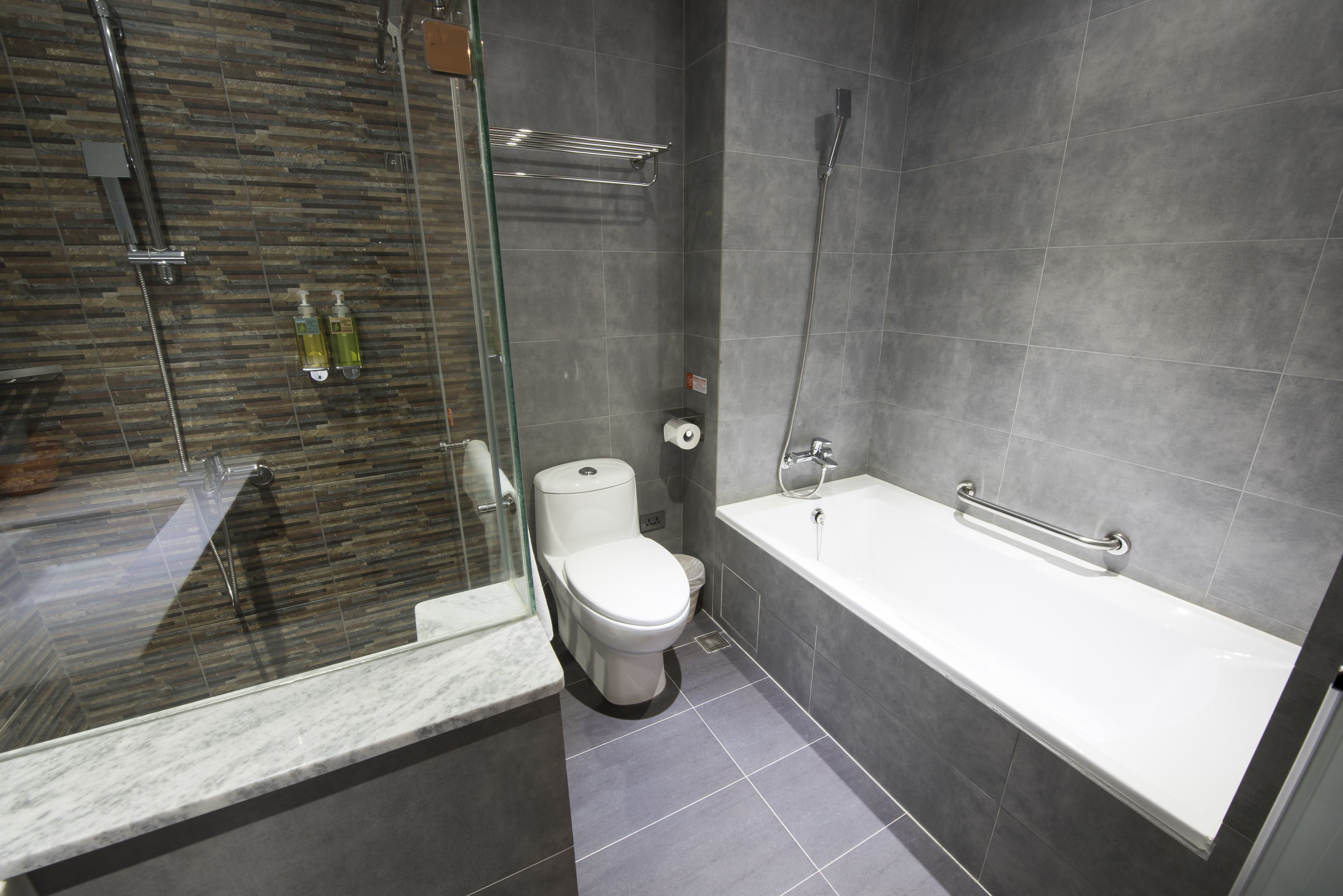 Un baño moderno con cabina de ducha de vidrio, inodoro blanco y bañera con barandilla.