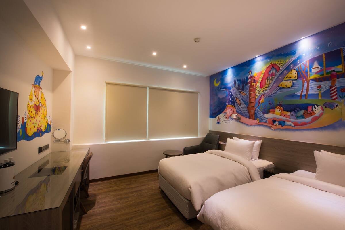 A hotel room with a large bed, a desk with a chair, a television, and a mural on the wall.