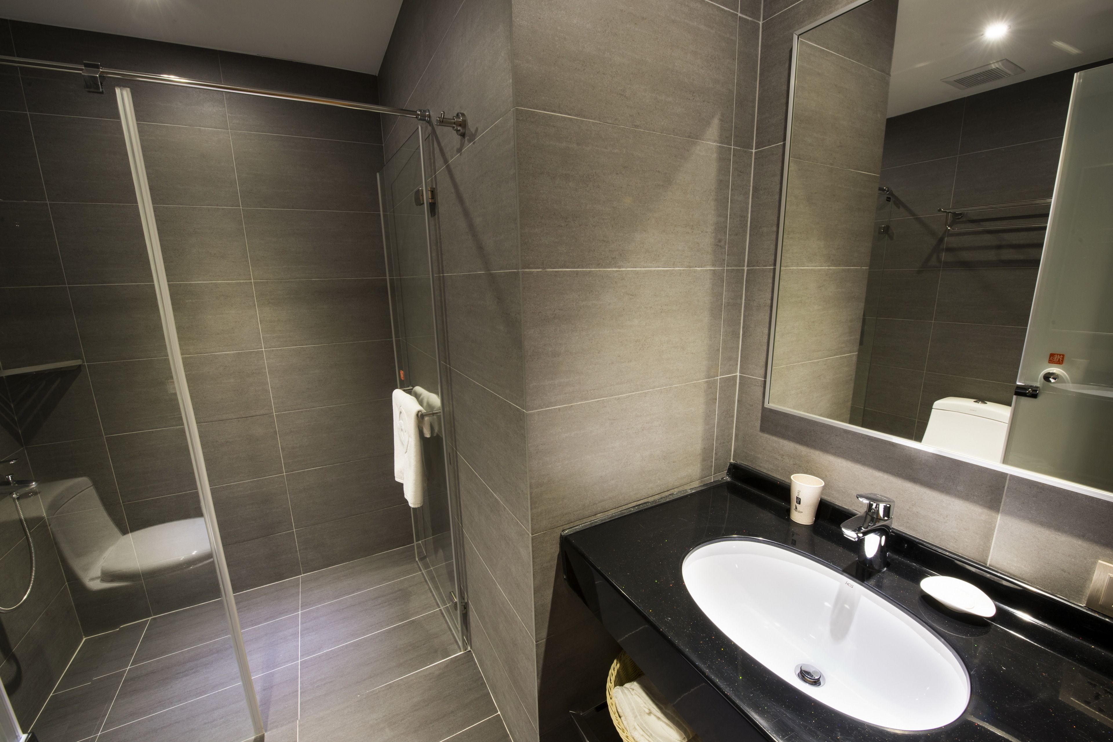 A modern bathroom with a glass-enclosed shower, a white sink, and a large mirror.