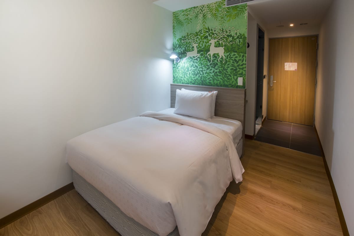 A hotel room with a bed, a green wall with a leaf pattern, and a wooden door.