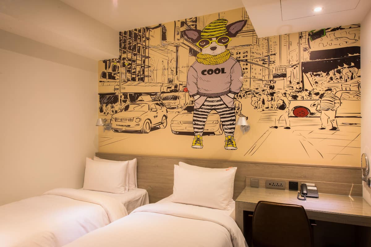 A hotel room with two beds, a desk, and a wall mural of a cartoon dog in a cityscape.