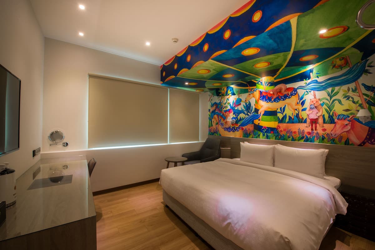 A modern hotel room with a large bed, a desk, and a vibrant mural on the wall.