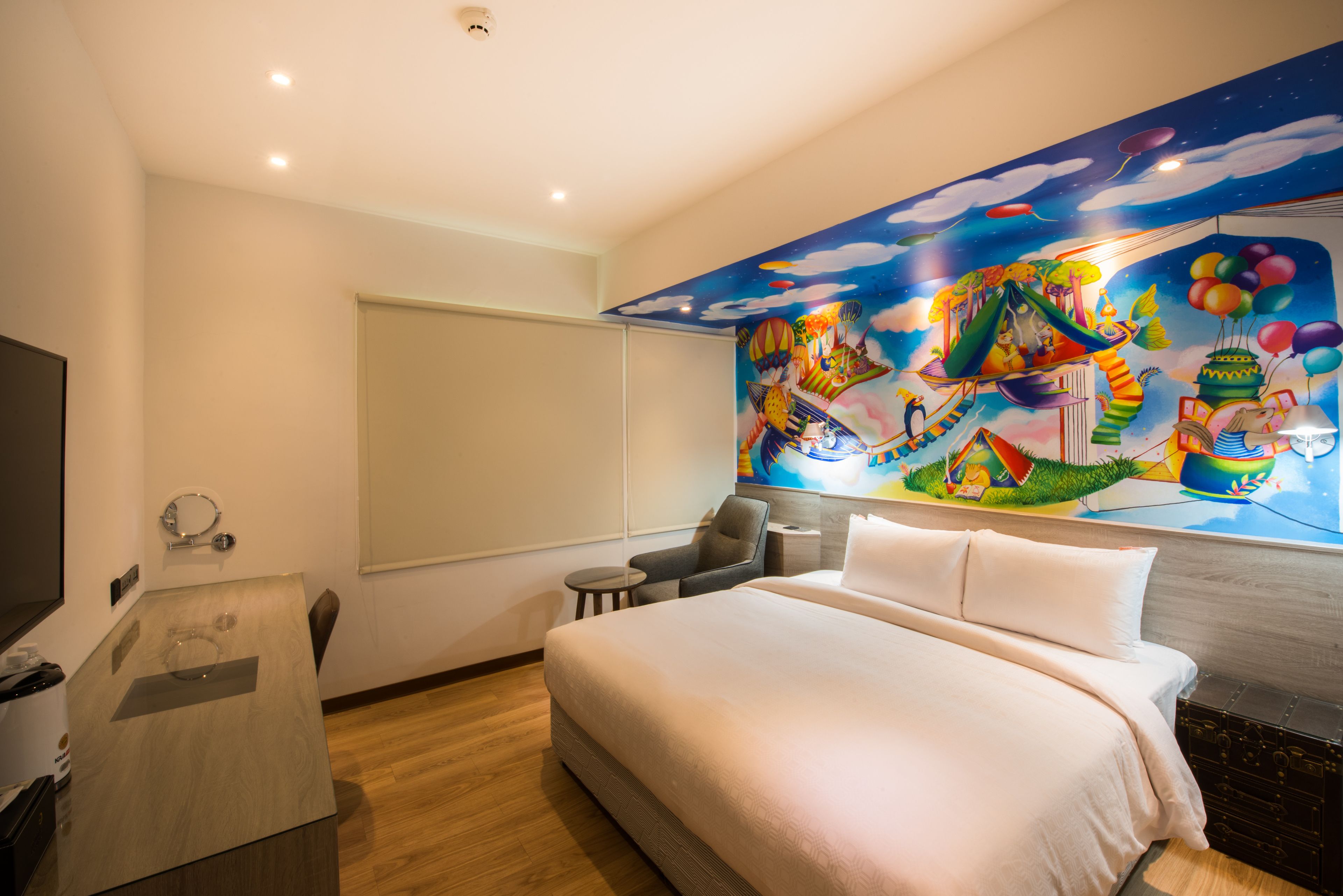 Una habitación de hotel con una cama grande, un escritorio con espejo, una pequeña mesa redonda y un mural colorido en la pared.