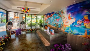 A reception area with a colorful mural, a wooden reception desk, and a bench with a plush toy. - Legend Hotel Pier 2 (Kaohsiung)