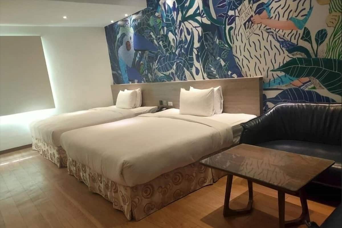 A hotel room with two beds, a sofa, a coffee table, and a large tropical-themed wall mural.